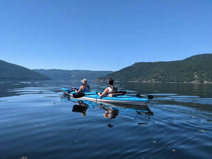 Zwei Jugendliche im Kajak auf ruhigem Wasser vor bewaldeten Hügeln