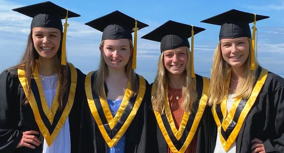 Quattro studentesse in toga da diploma si trovano davanti a un cielo blu nel campus del Collingwood Collegiate Institute.