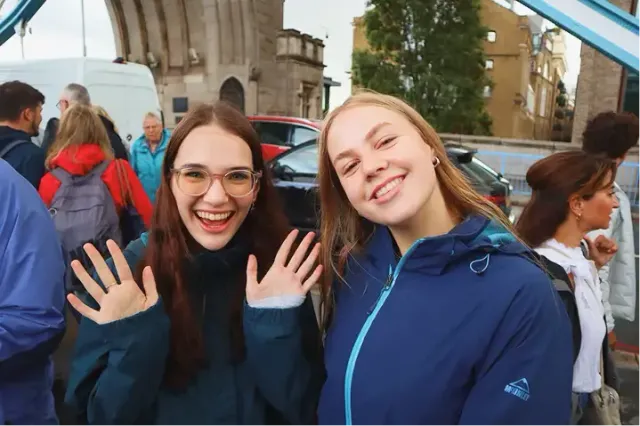 Due studentesse sorridenti salutano con la mano in una strada cittadina durante un soggiorno all'estero