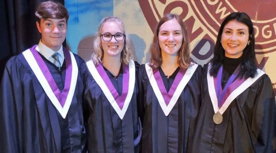 Quattro studenti della Thousand Islands Secondary School in toga da diploma sono in piedi davanti a uno sfondo colorato con il logo dell'università.