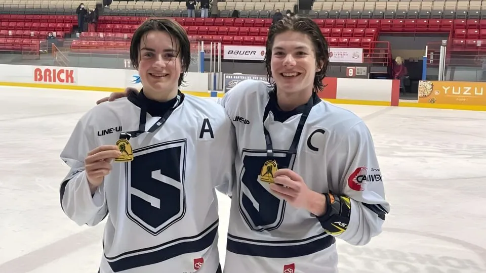 Due studenti del College Saint-Bernard stanno in piedi con le medaglie sul ghiaccio di una pista da hockey.