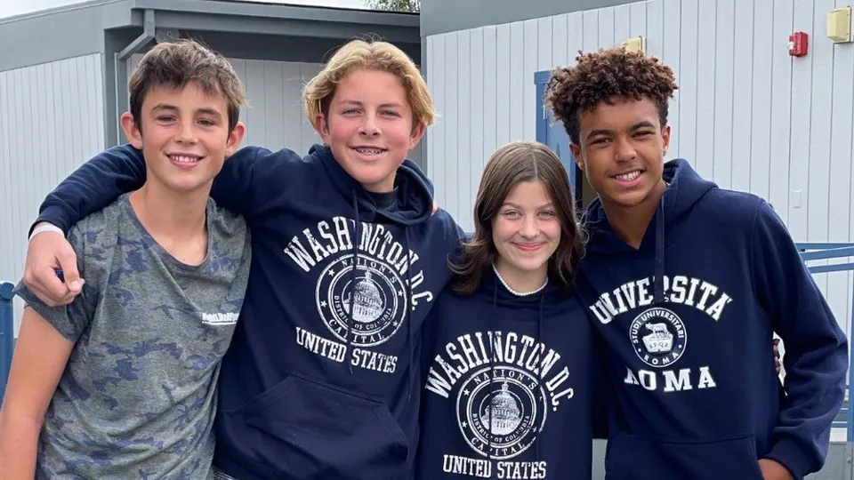 Quattro studenti e studentesse si trovano davanti all'edificio della Coastal Christian School e sorridono alla telecamera.