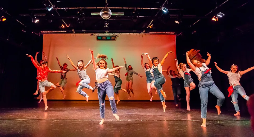 Studenti del Havant College si esibiscono in una dinamica performance di danza su un palco con luci colorate.