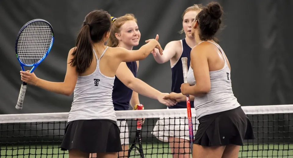 Tre studentesse in abbigliamento sportivo parlano tra loro con le racchette da tennis in mano sul campo da tennis del Braemar College.