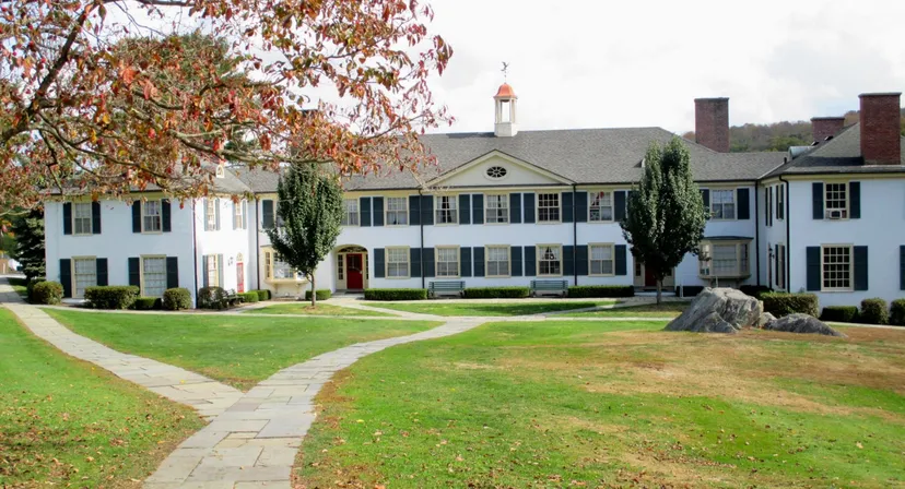 L'edificio bianco in stile coloniale con il tetto rosso della The Frederick Gunn School si erge su un prato curato circondato da alberi autunnali.