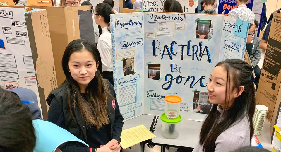Due studentesse della Richmond Secondary School sono in piedi davanti a un tabellone informativo sui batteri con materiali scientifici.