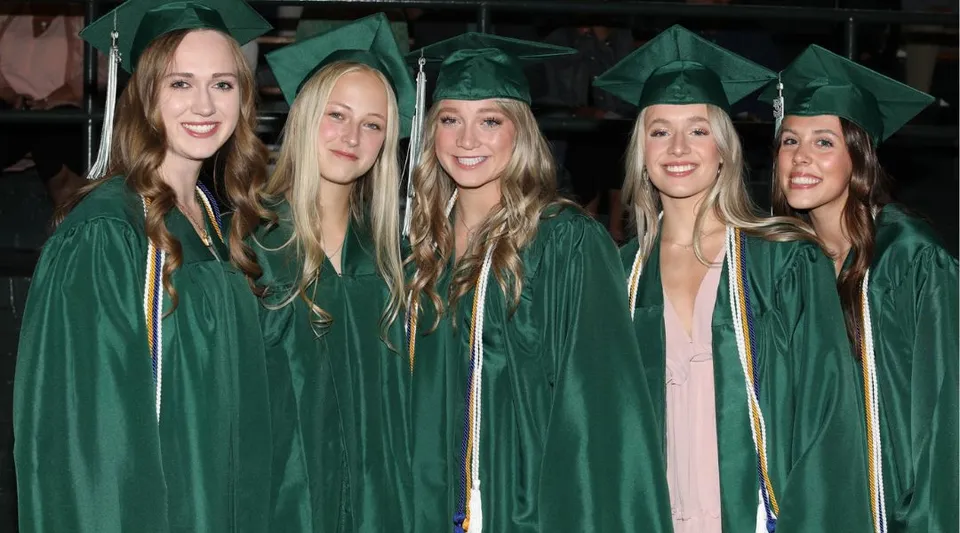 Cinque studentesse della Billings Central Catholic High School festeggiano insieme il loro diploma indossando toghe verdi.