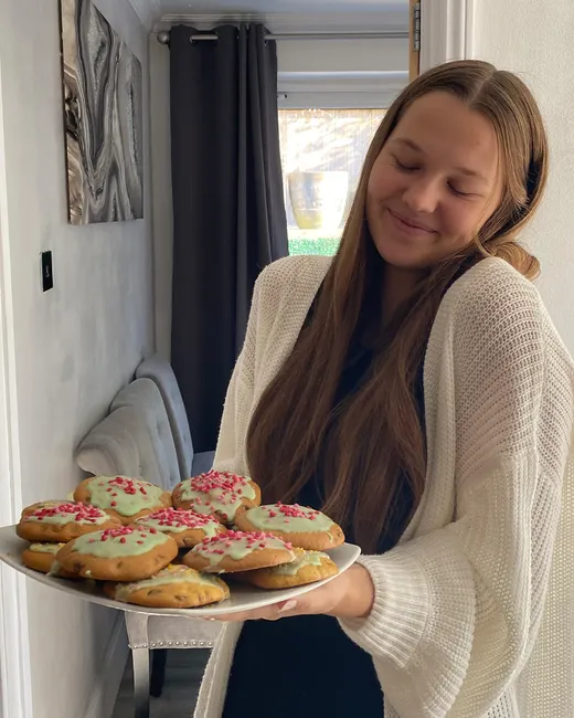 Estudiante muestra sonriente una bandeja de galletas decoradas caseras