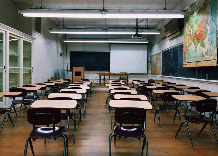 Leeres Klassenzimmer mit Einzeltischen, Tafeln, Leinwand und Landkarte an der Wand