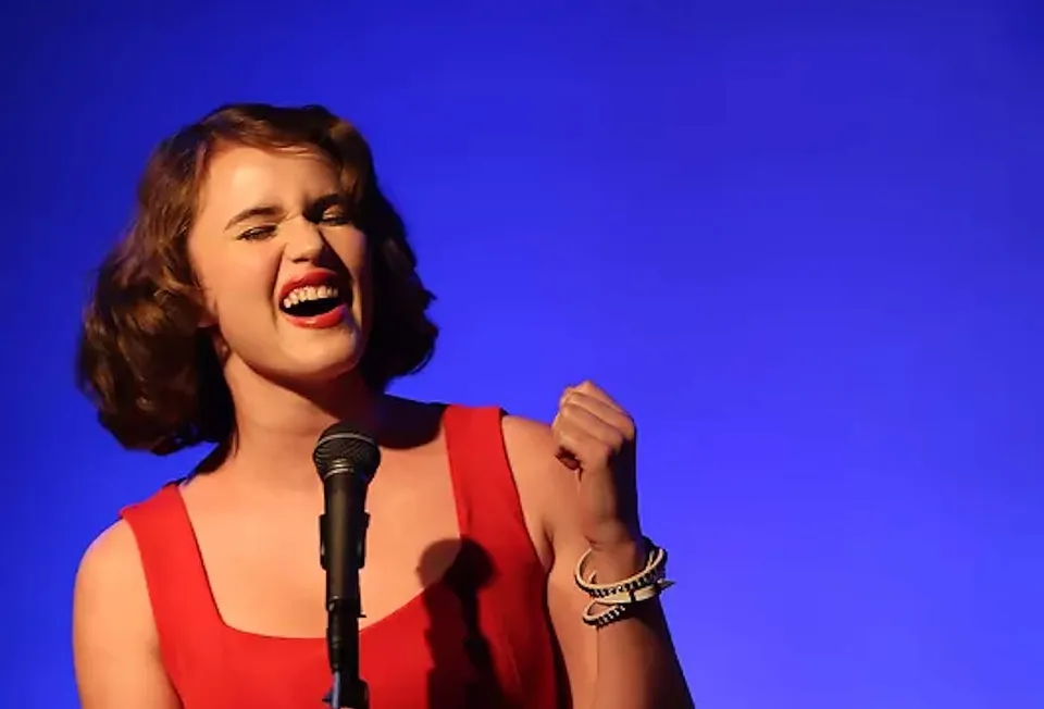 Una studentessa della Arroyo Pacific Academy canta con passione in un microfono su sfondo blu.