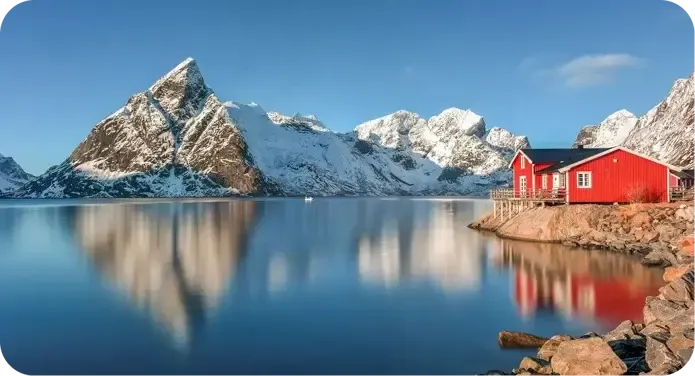 Vorschaubild zum Film über Norwegen: rotes Holzhaus am Fjord vor verschneiten Bergen