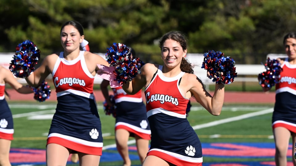 La squadra di cheerleading della St. John the Baptist High School attraversa il campo con i pompon.