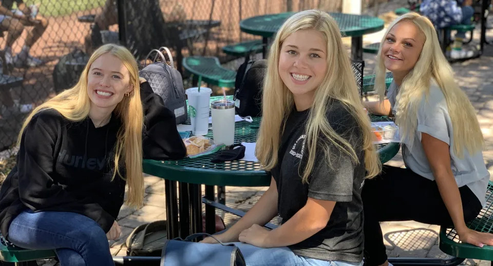 Tre studentesse con lunghi capelli biondi sedute a un tavolo all'aperto nel campus della Orangewood Christian School.