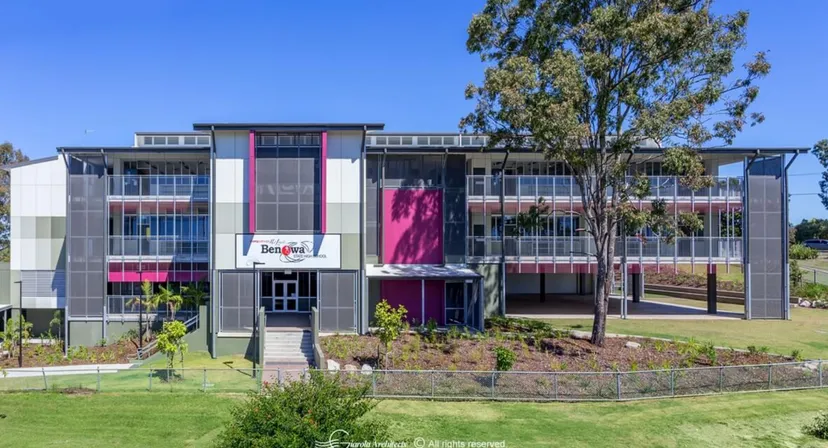 L'edificio moderno a più piani con pareti rosa e grigie della Benowa State High School si trova su un'area verde ben curata circondata da alberi.