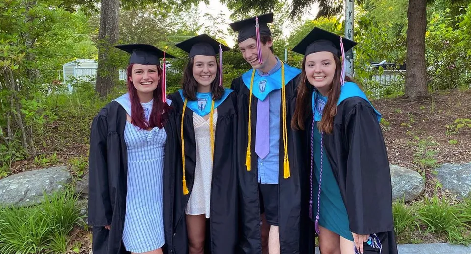 Un gruppo di quattro giovani donne in abito da diploma si trova nel verde del campus della Camden Hills Regional High School.