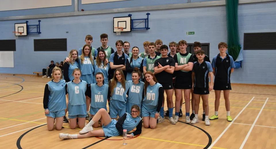 Un gruppo di studenti del Prior Park College posa nella palestra con canestri da basket sullo sfondo.
