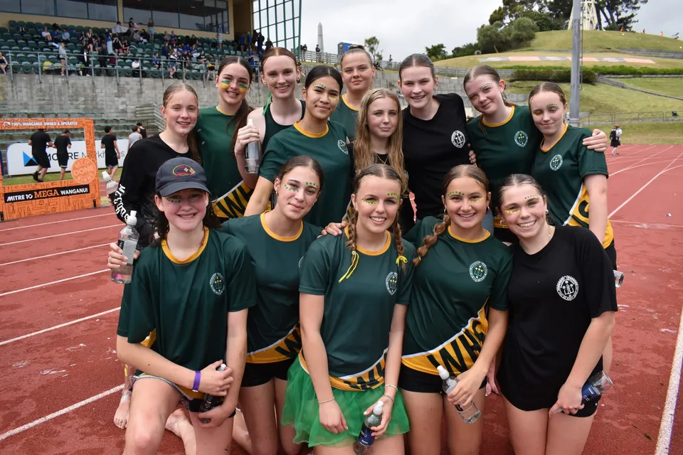 Un gruppo di giovani atlete posa con maglie verdi e gialle sul campo sportivo del Whanganui Girls’ College.
