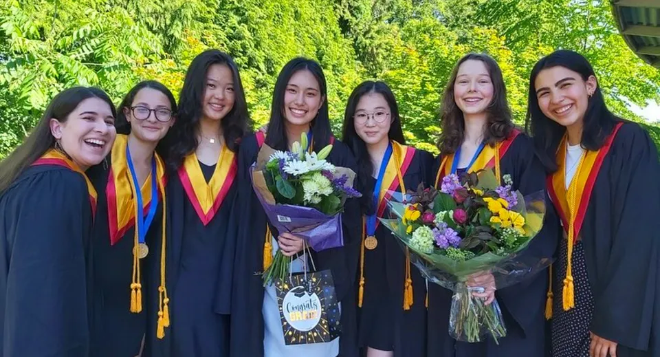 Un gruppo di diplomate della West Vancouver Secondary è posizionato con mazzi di fiori davanti a uno sfondo verde.