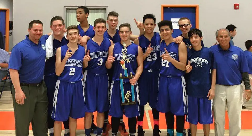 Un gruppo di studentesse e studenti di basket della Apple Valley Christian School in maglie blu posa in una palestra.