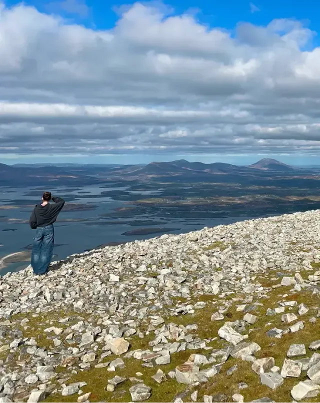 Ragazzo su una cima rocciosa osserva il panorama su laghi e colline in Irlanda