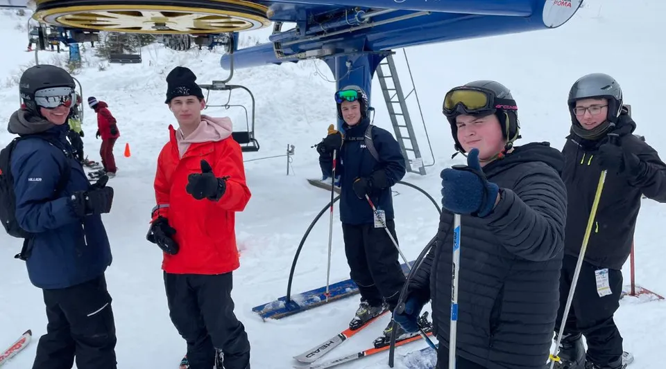 Un gruppo di studenti della Queen Elizabeth Regional High in abbigliamento invernale si trova presso lo skilift su una montagna innevata.