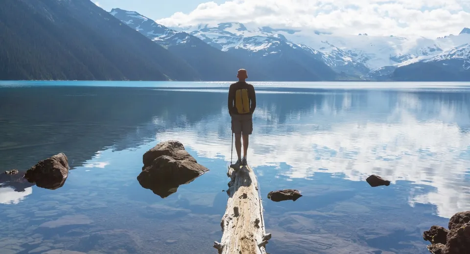 Un singolo studente si trova su un pontile di legno davanti a un lago specchiato con montagne innevate sullo sfondo nel campus della Harbour View High School.
