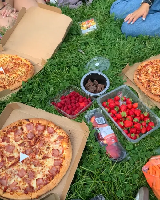 Picnic sobre la hierba con pizzas, fresas y frambuesas compartidas entre amigos