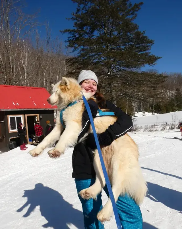 Studentessa sorridente tiene in braccio un grande cane husky nella neve durante un anno all'estero in Canada