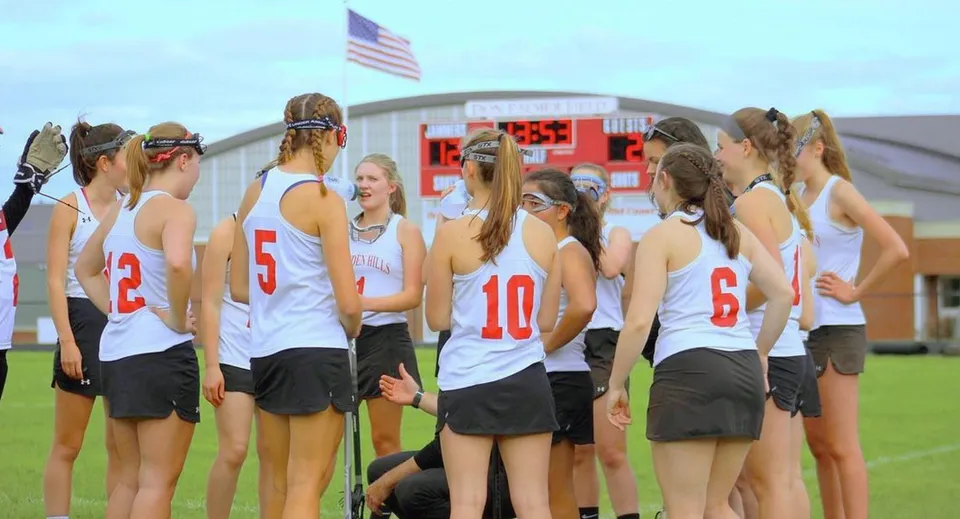 Un gruppo di giovani atlete si trova sul campo sportivo della Camden Hills Regional High School con una bandiera americana sullo sfondo.