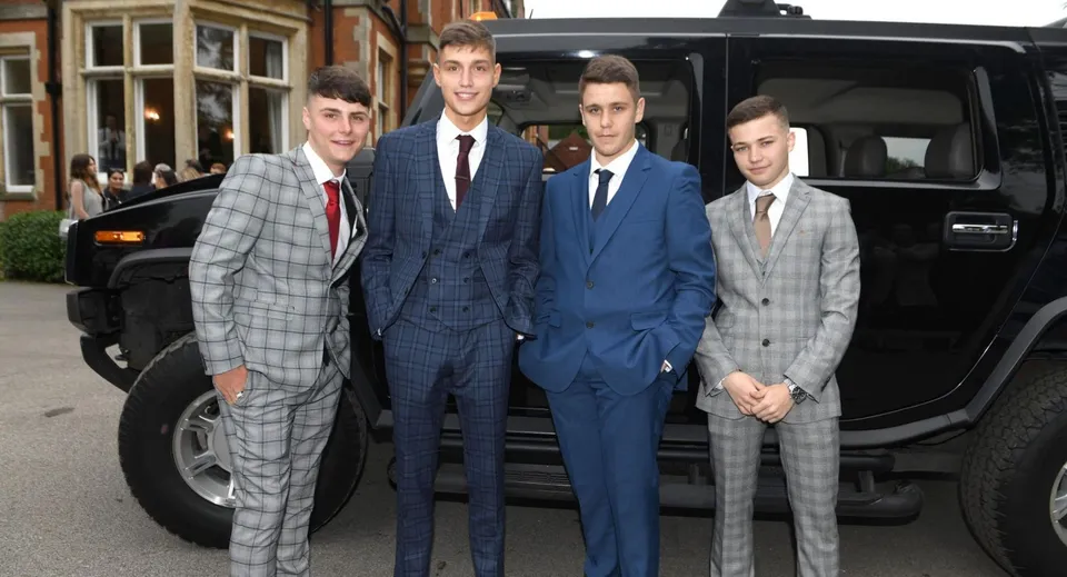 Un gruppo di studenti della Whitgift School in abito elegante si trova davanti a un grande veicolo nero lungo una strada cittadina.