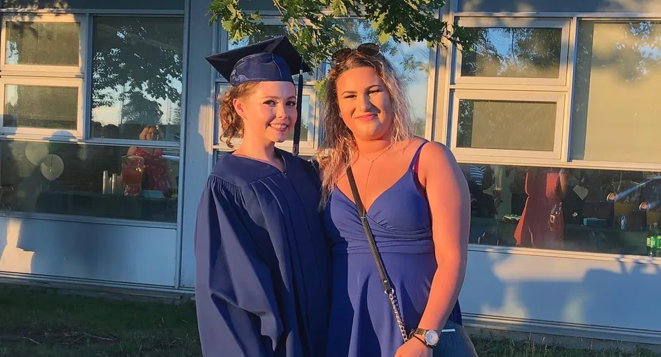 Due studentesse, una con la toga da diploma, sono in piedi davanti all'edificio del Stayner Collegiate Institute.