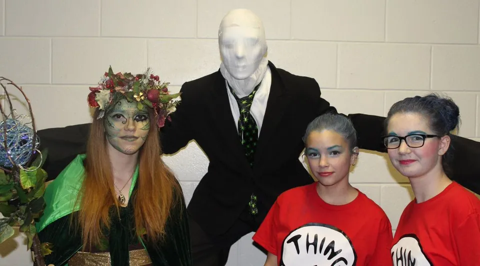 Tre studentesse della St. James' Regional High posano in costumi vivaci e stravaganti davanti a una parete piastrellata.