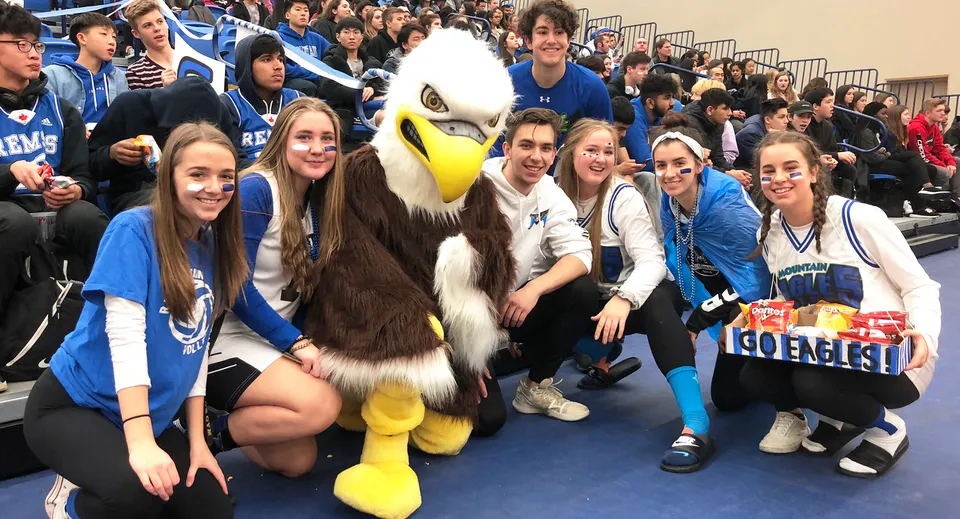Studenti e studentesse della R.E. Mountain Secondary School posano con la grande mascotte durante un evento scolastico.