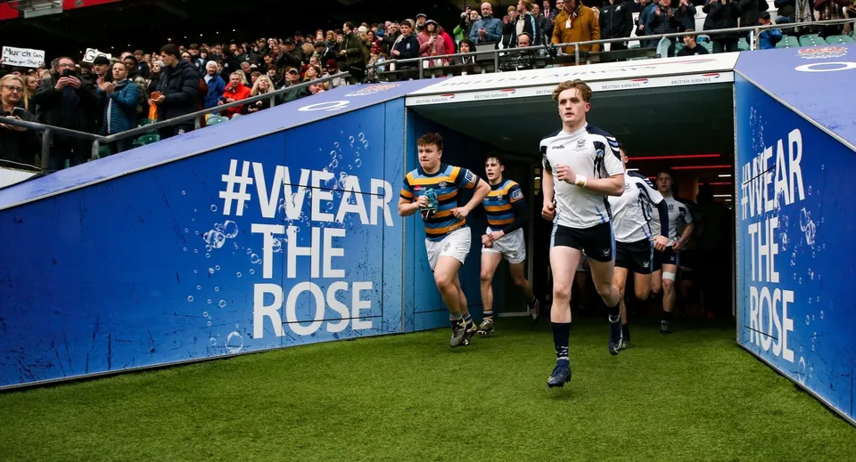 Studenti della Sutton Valence School camminano su un campo con un grande striscione #WearTheRose in primo piano.