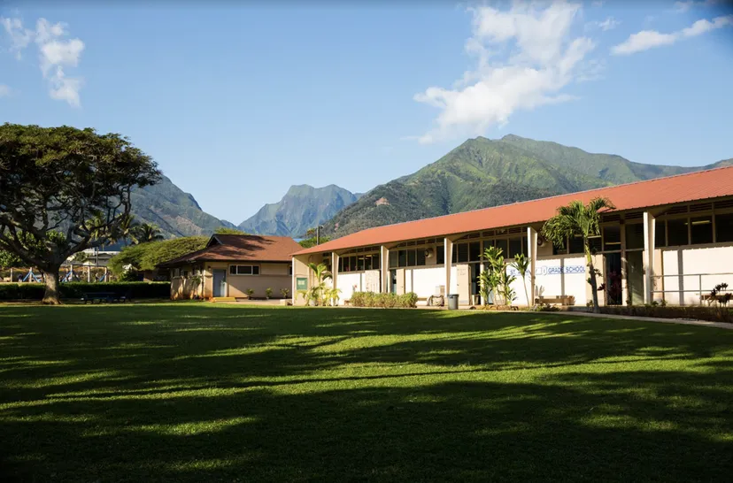 Un prato verde davanti a edifici colorati con uno sfondo di montagne nel campus della St. Anthony School.