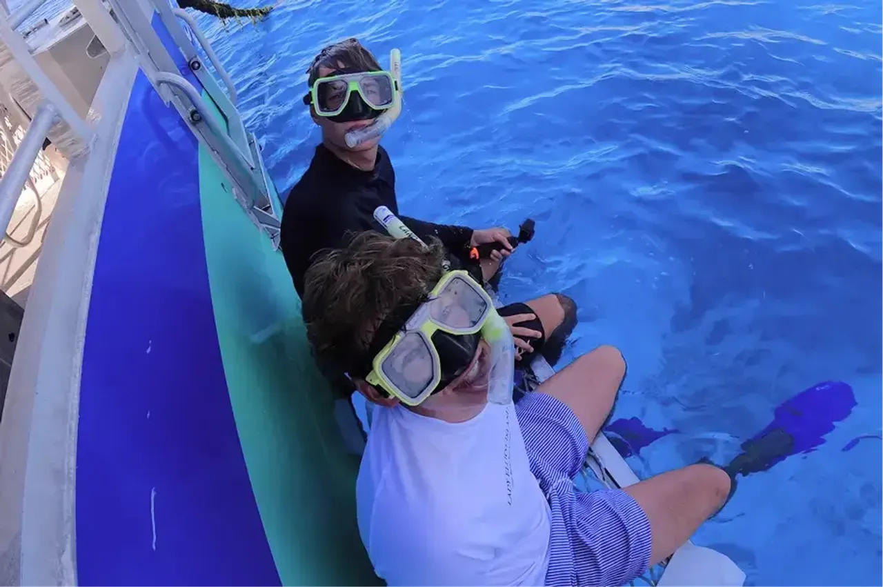 Due ragazzi con maschere da snorkeling seduti sul bordo di una barca