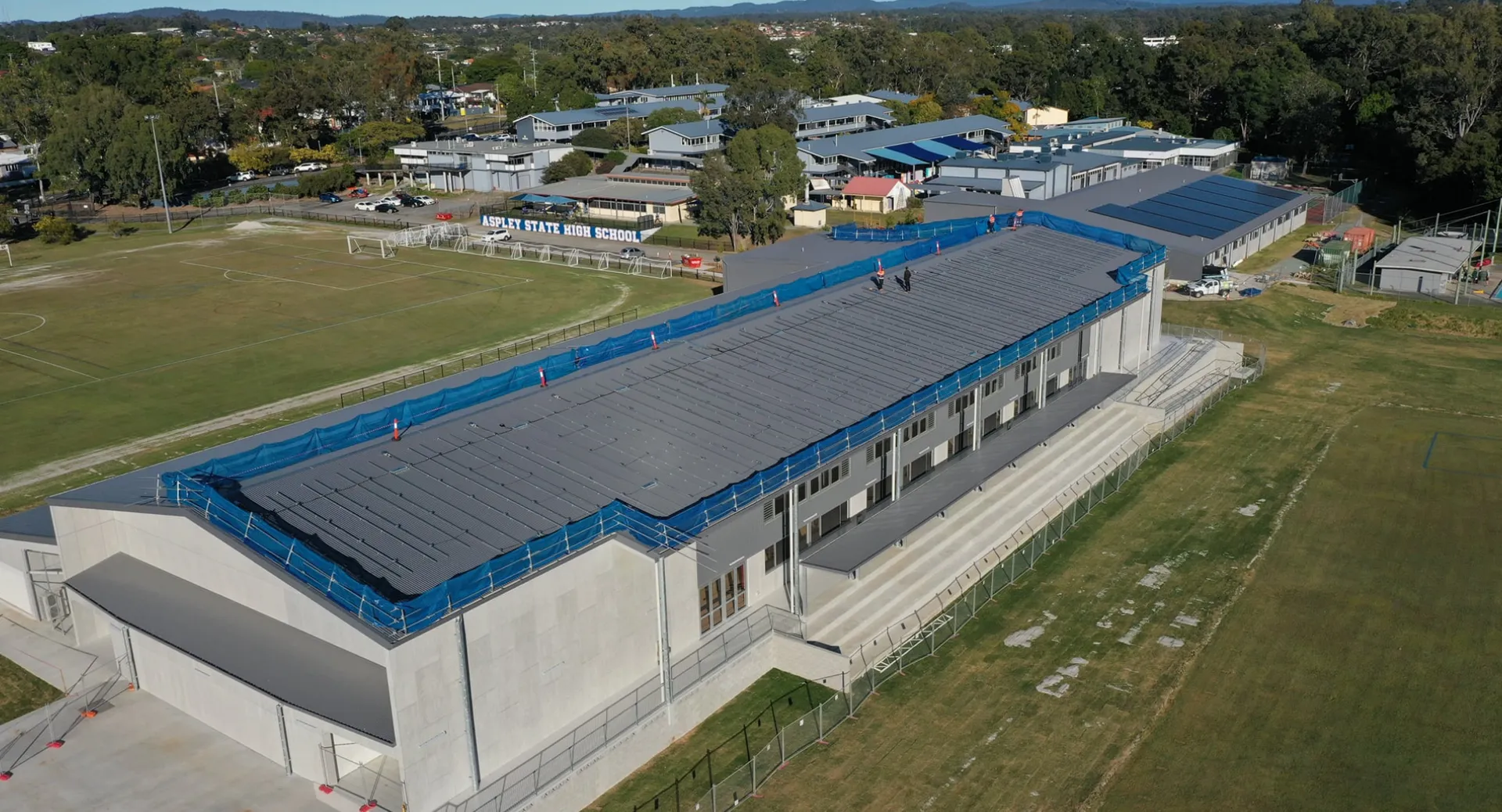 L'edificio moderno della Aspley State High School si trova davanti a un'area verde con case e montagne sullo sfondo.