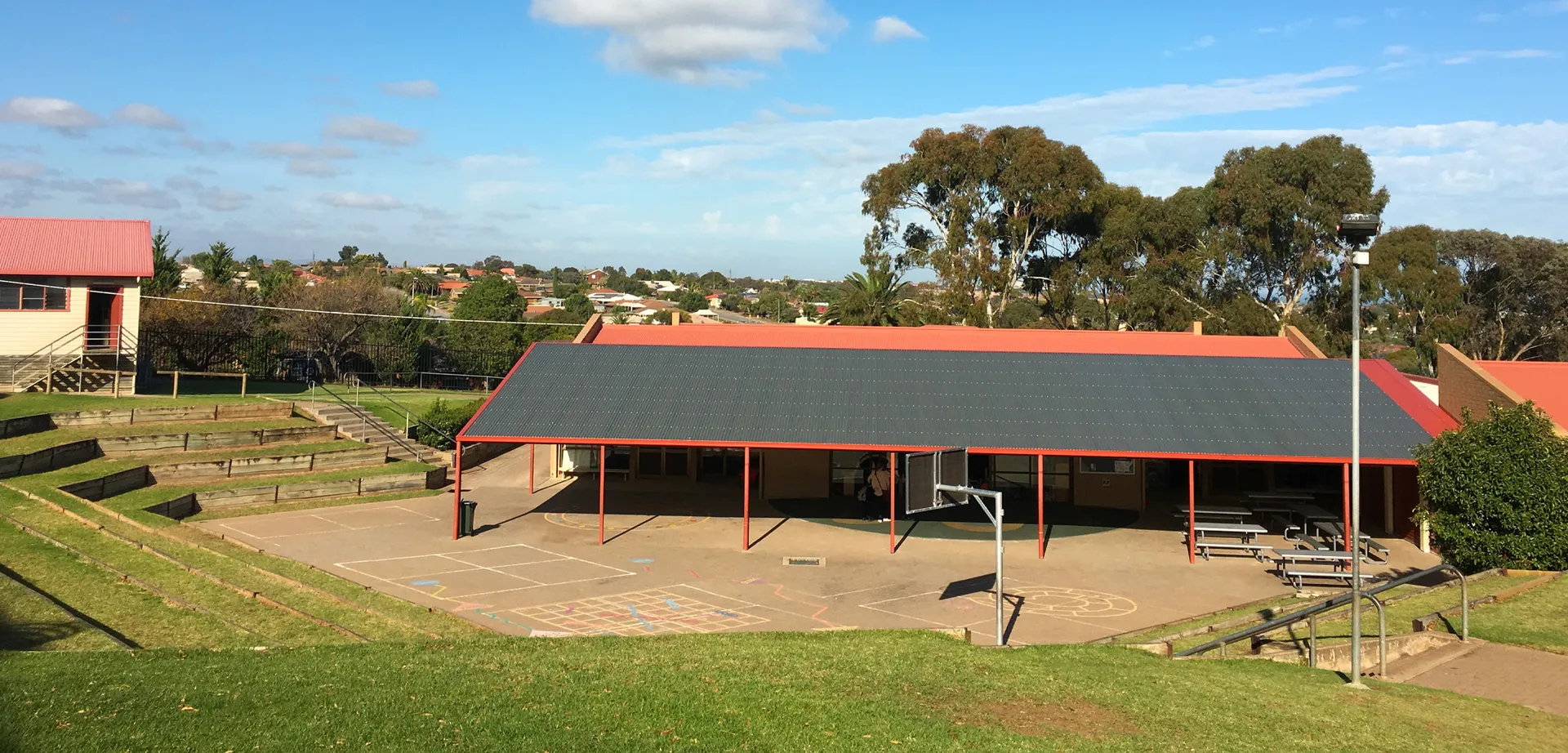 Un'area verde all'aperto con una zona coperta nel campus della Hallett Cove School sotto un cielo blu.