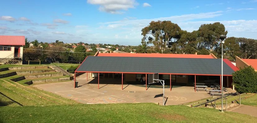 Un'area verde all'aperto con una zona coperta nel campus della Hallett Cove School sotto un cielo blu.
