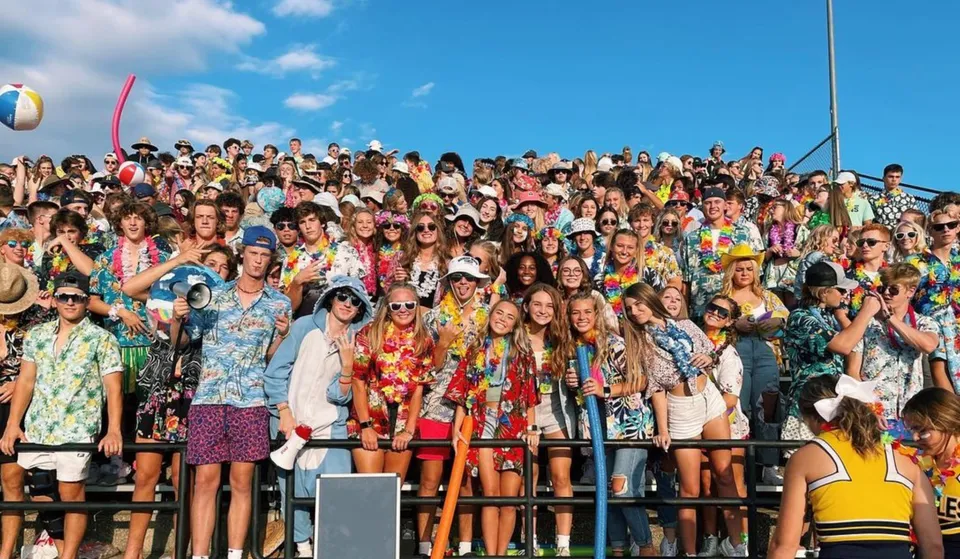 Un grande gruppo di persone si riunisce all'aperto sotto un cielo terso nel campus della Jenison High School.