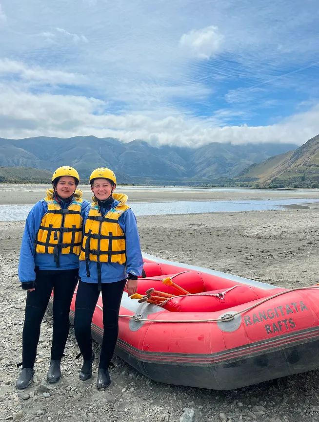 Due studentesse in tenuta da rafting accanto a un gommone in Nuova Zelanda