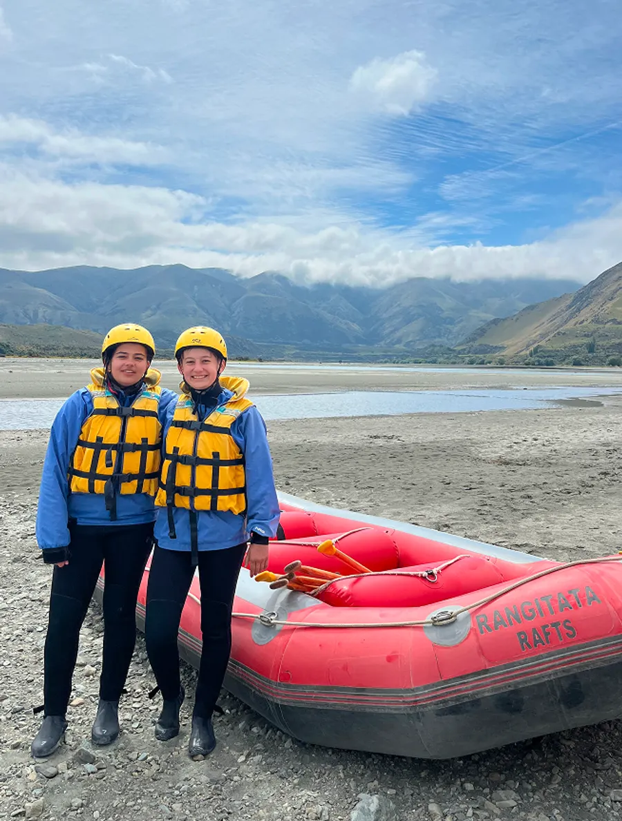 Due studentesse in tenuta da rafting accanto a un gommone in Nuova Zelanda