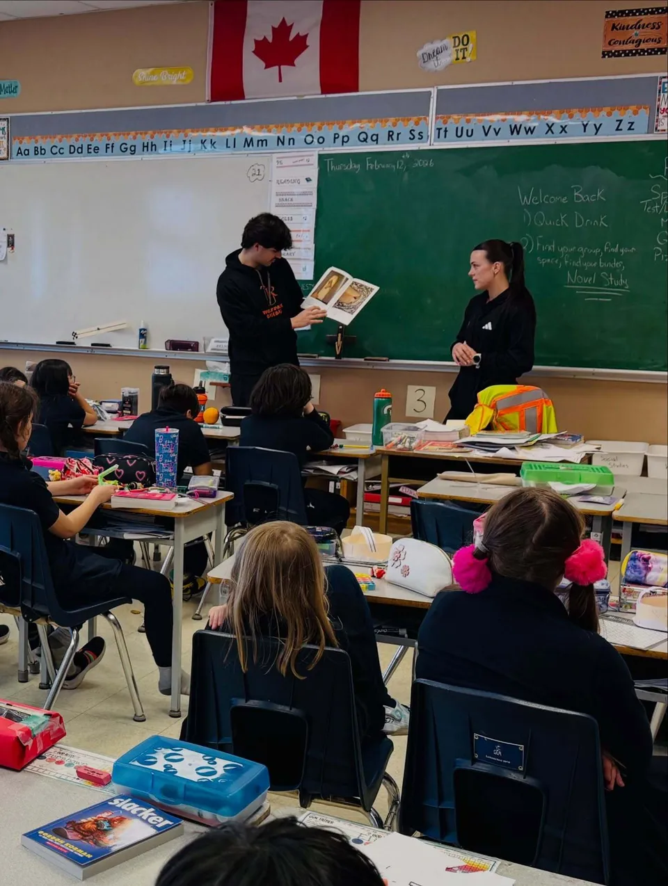 Uno studente mostra un libro aperto davanti alla lavagna in un'aula della St Ann's Academy accanto all'insegnante.