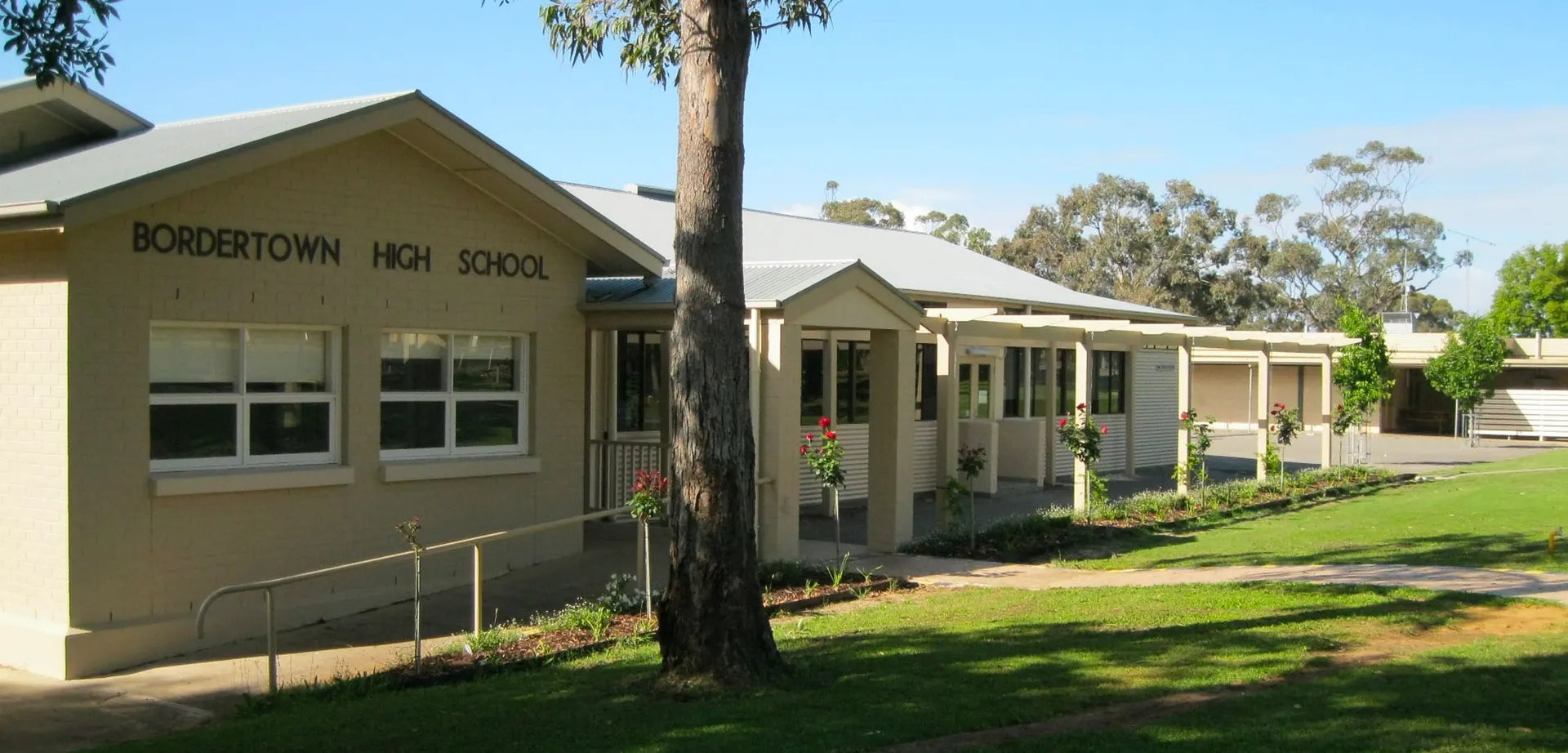 L'edificio scolastico ad un piano della Bordertown High School si trova dietro una palma su un'area erbosa.