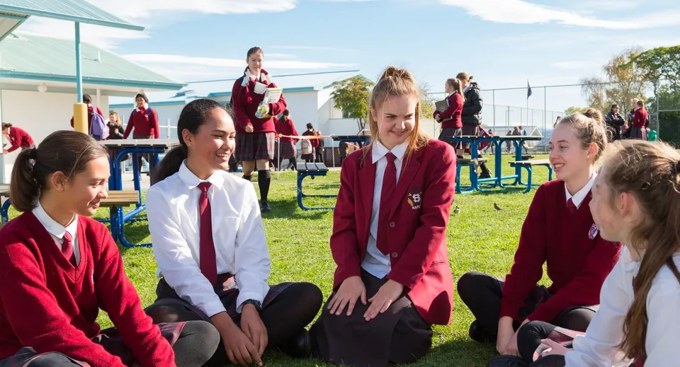 Studentesse e studenti del Sacred Heart College Napier seduti all'aperto sull'erba davanti a un edificio scolastico.