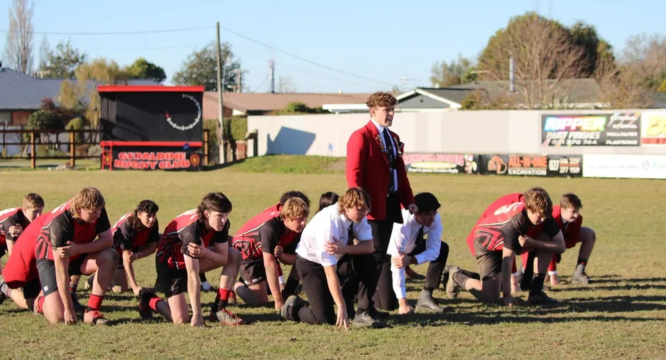 Un gruppo di studentesse e studenti della Geraldine High School si raccoglie sul campo sportivo davanti a un rimorchio rosso e ad alcuni edifici.