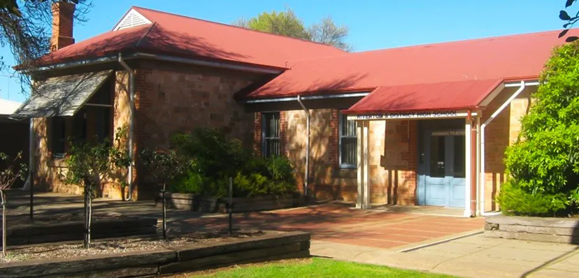 L'edificio in stile adobe con tetto in tegole rosse si trova nel campus della Riverton and District High School, circondato dal verde.