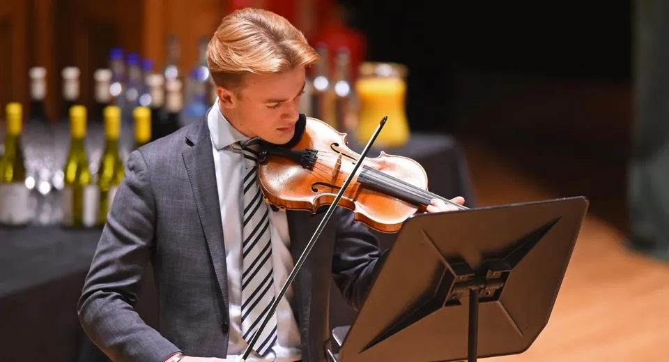 Uno studente di Earlscliffe in giacca e cravatta suona il violino davanti a un leggio.