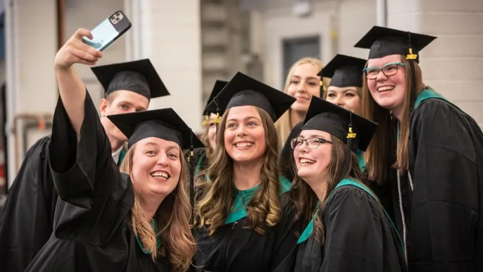 Un gruppo di diplomati del Lethbridge Collegiate Institute posa in abito da cerimonia davanti a un edificio universitario.