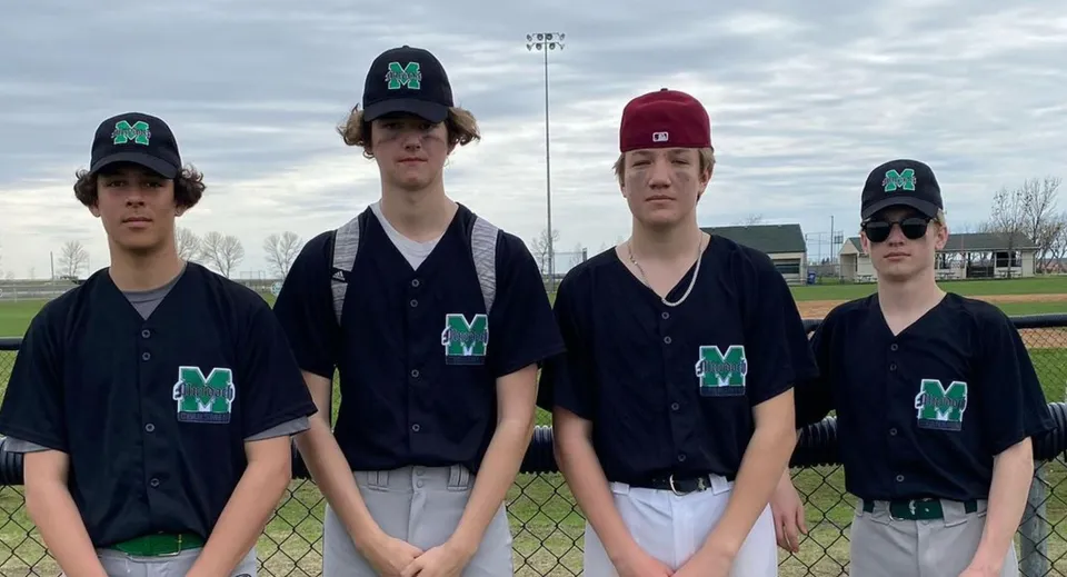 Un gruppo di studenti e studentesse che giocano a baseball in divisa si trova sul campo da baseball del Murdoch Mackay Collegiate sotto un cielo nuvoloso.